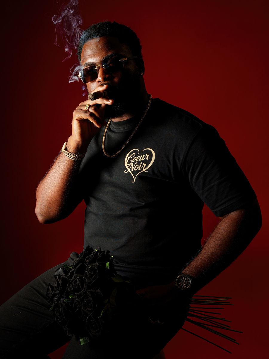 Model wearing the Cœur Noir Cœur Brodé tee, gold script embroidery, oxblood studio backdrop